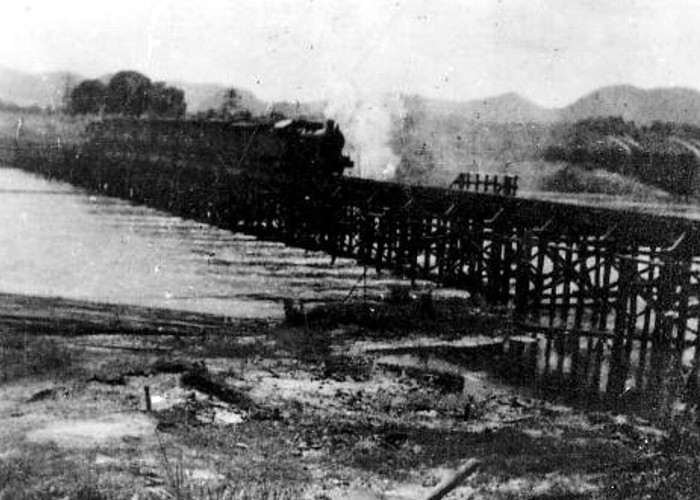 widok na drewniany most na rzece Khwae Yai. W tle widoczne zarysy mostu betonowego.