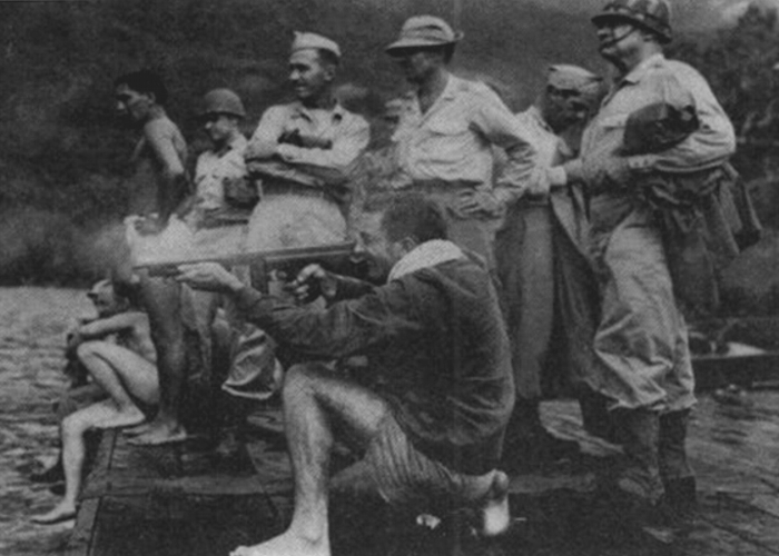 Instruktor strzelania, Roland Peterson, strzela z pistoletu maszynowego Thompson podczas szkolenia, a dowodzący Zwiadowcami Alamo Frederick Bradshaw (w środku, podparty pod boki) i genrał Innis Swift (po prawej w hełmie) przygląda się. Wyspa Fergusonna, styczeń 1944 roku.