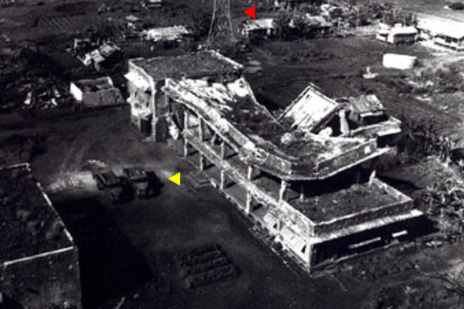 Zniszczone japońskie centrum dowodzenia na wyspie Eten. Widoczne poważne uszkodzenie dachu spowodowane bezpośrednim trafieniem bombą lotniczą. Na lewo od budynku widoczne dwie ciężarówki (strzałka czerwona) o raz antena stacji radiowej (strzałka żółta)